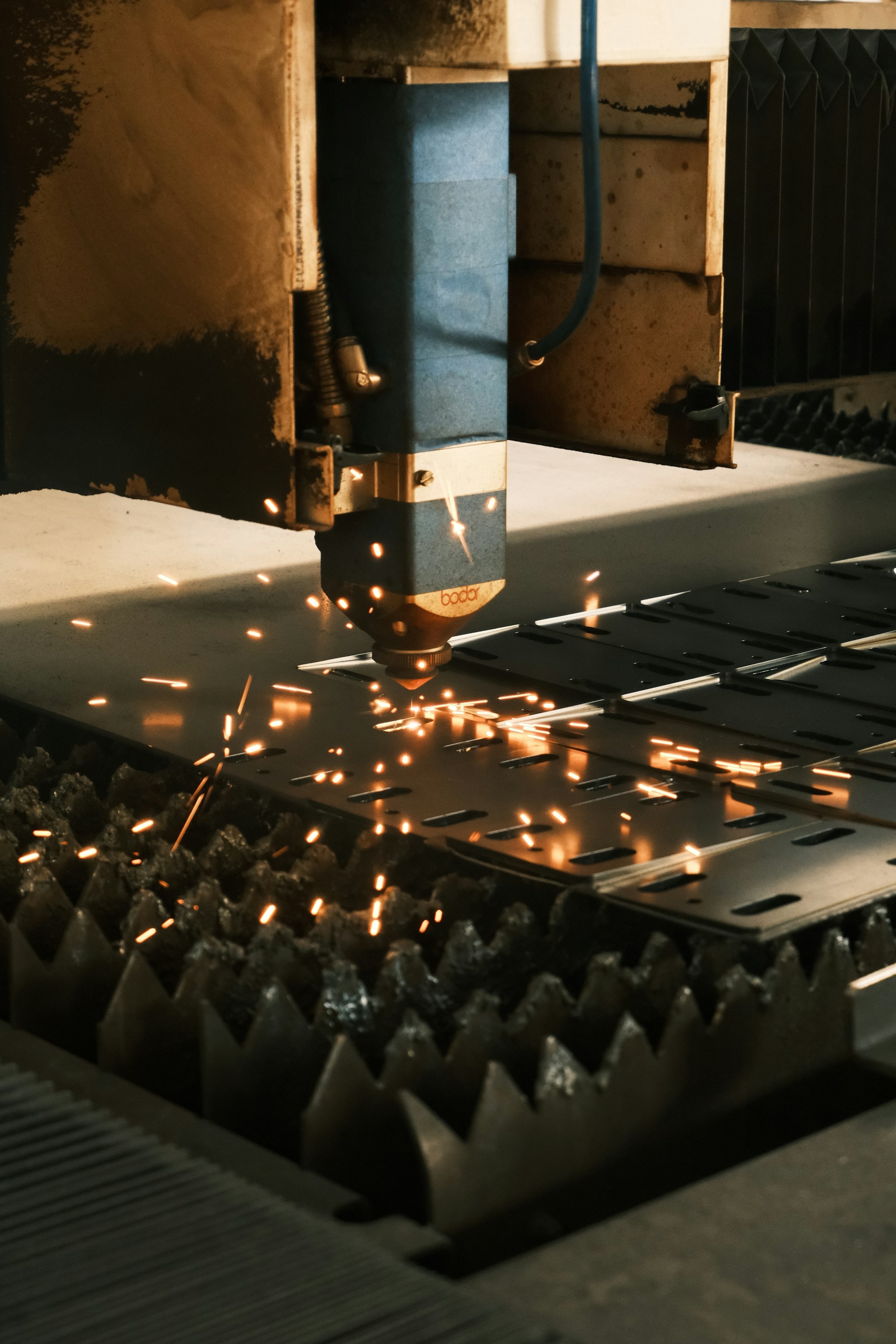 Głowica lasera wycinająca elementy w metalowej blasze, rozświetlona iskrami